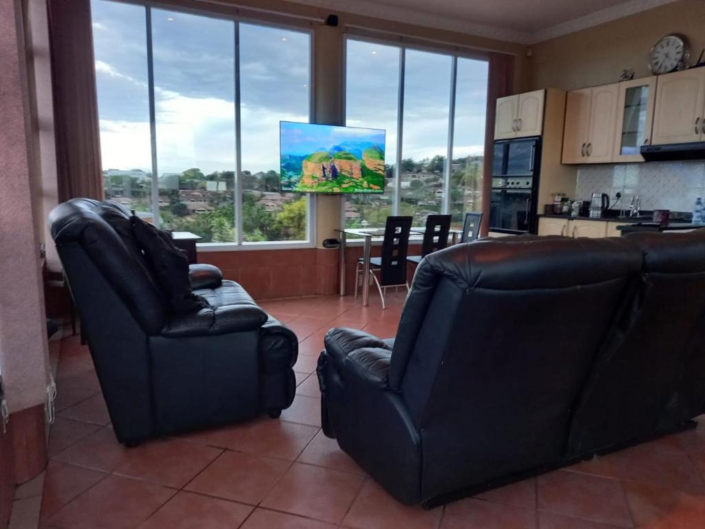 a living room with two black chairs and a kitchen at La Lucia Ridge Self Catering Penthouse Environment in Durban