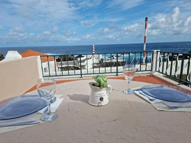 uma mesa com dois copos de vinho numa varanda em "Apartamentos do Farol" com vista para o mar em Santa Cruz das Flores