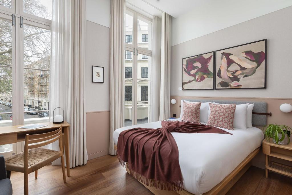 a bedroom with a bed and a desk and windows at Inhabit Queen's Gardens, a Member of Design Hotels in London