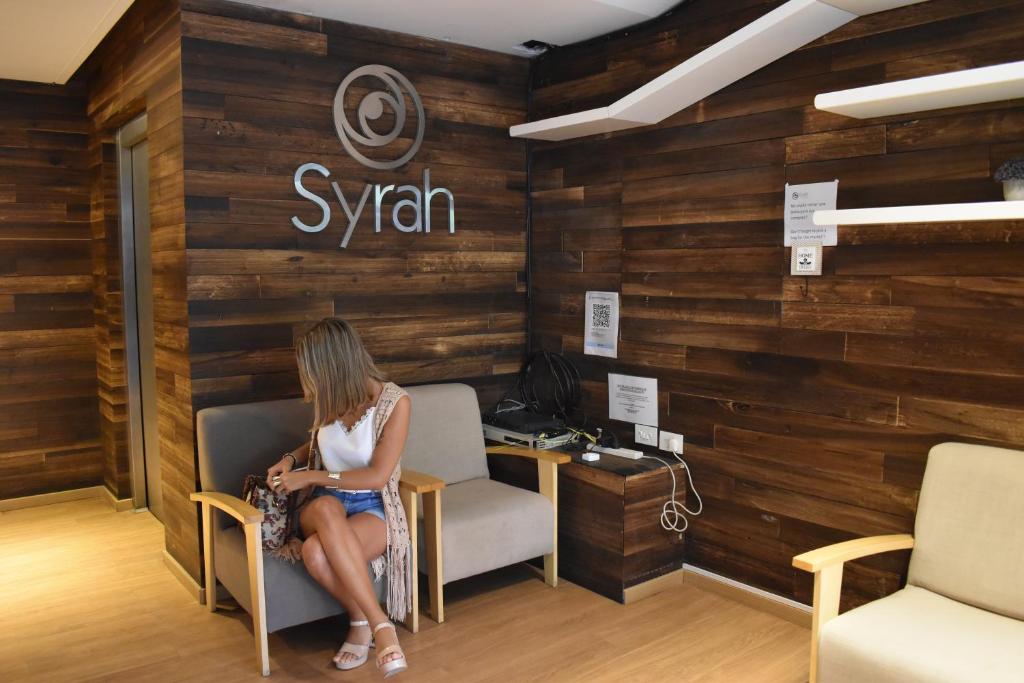 Una donna seduta su una sedia in una stanza con un cartello di Syrah Suites a Buenos Aires