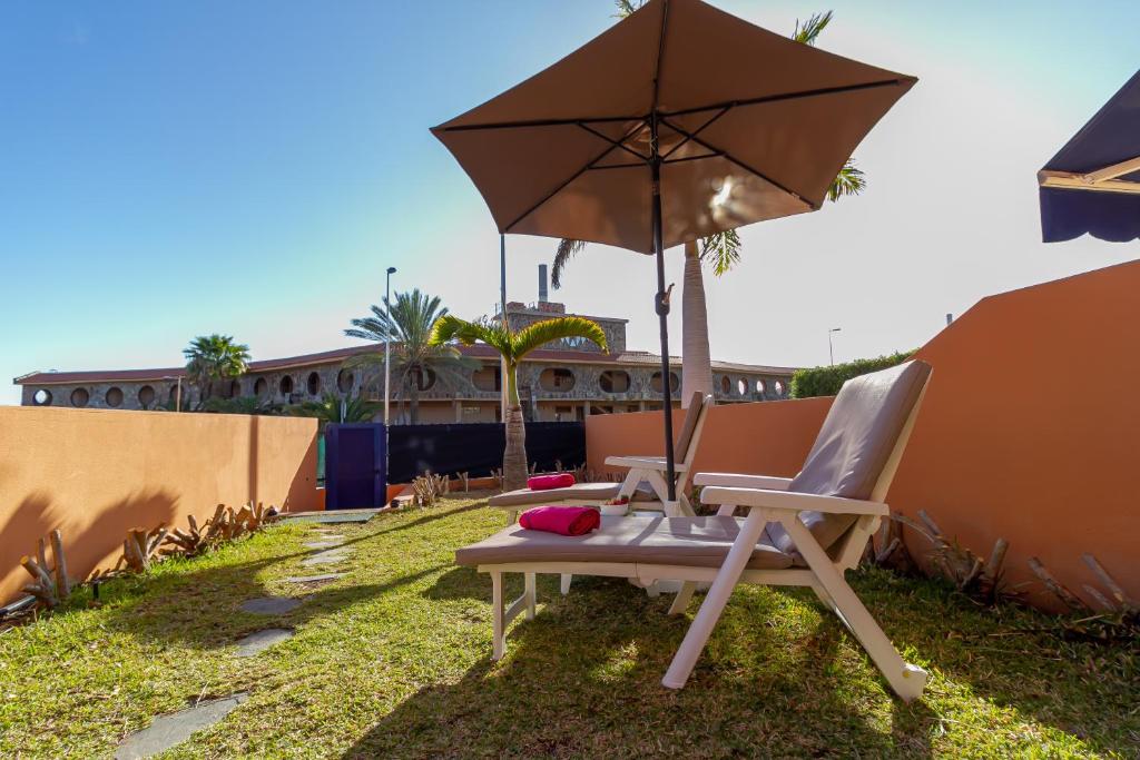 una silla con un paraguas sentado en el césped en Duplex Meloneras with Free Wifi and private Garden en Meloneras