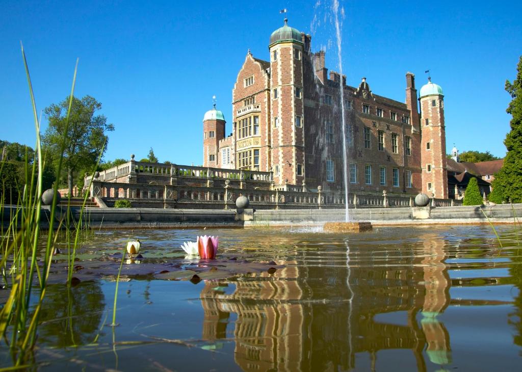 um grande edifício com um lago em frente em Madingley Hall em Cambridge