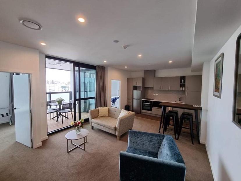 a living room with a couch and a table and a kitchen at Modern, Central City, Penthouse Floor Apartment. in Auckland