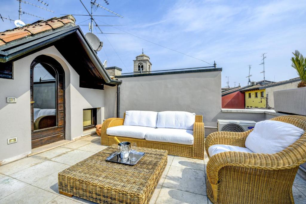 un patio con sedie in vimini e un divano sul balcone. di Prestige Suite Sirmione a Sirmione