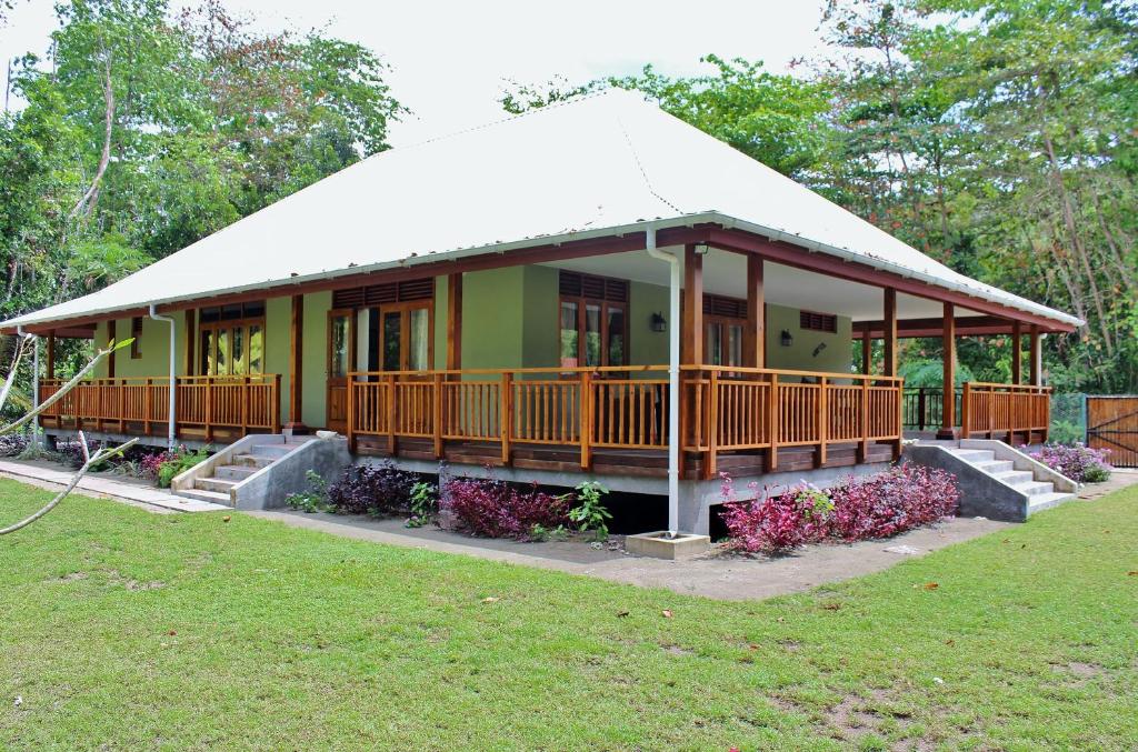 a green house with a porch and a grass field at Casa Verde in Grand'Anse Praslin