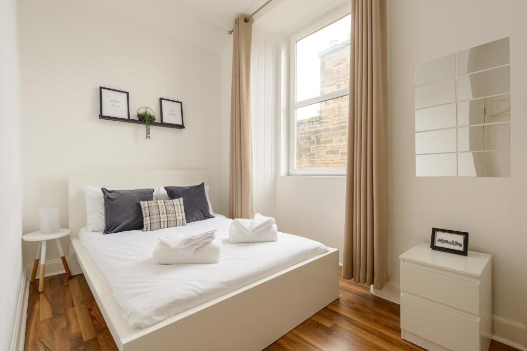 a white bedroom with a large white bed and a window at The London Road Apartment - 2BR/1BA in Edinburgh