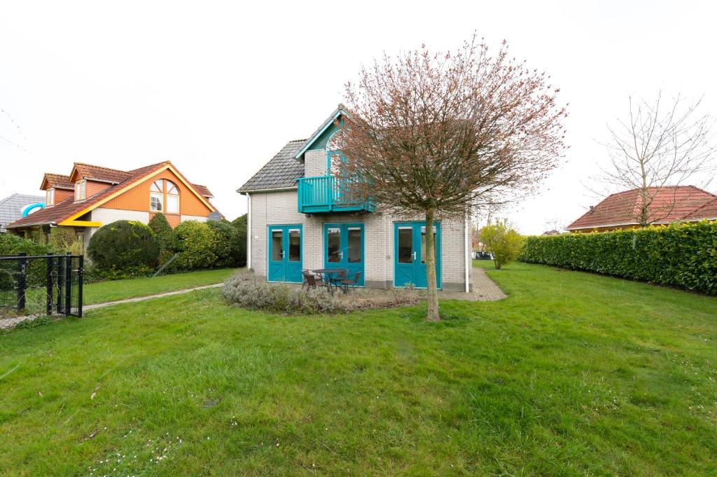 een blauw-wit huis met een boom in een tuin bij Fréjus 110 - Kustpark Village Scaldia in Hoofdplaat