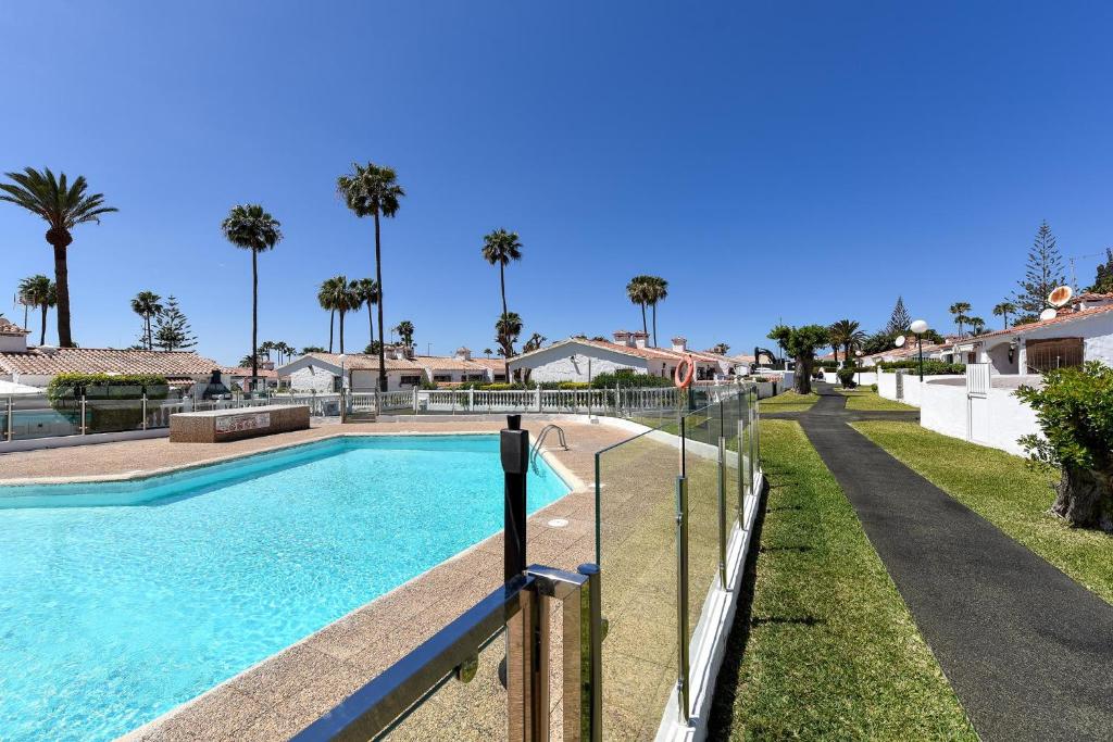 a swimming pool with a fence and palm trees at Bungalow Santa Barbara EMC2 by VillaGranCanaria in Playa del Ingles