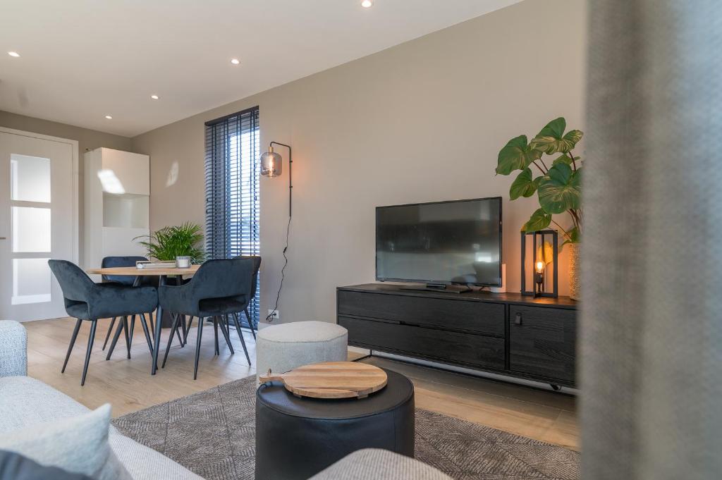 een woonkamer met een televisie en een tafel met stoelen bij Luxe appartement dichtbij strand en zee, in het hart van de bollenstreek in Noordwijkerhout