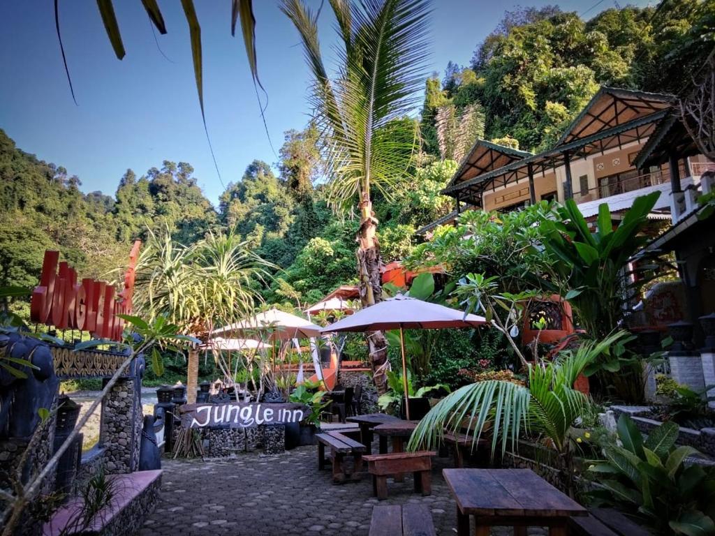 un patio con mesas y sombrillas en un complejo en Jungle Inn Bukit lawang en Bukit Lawang