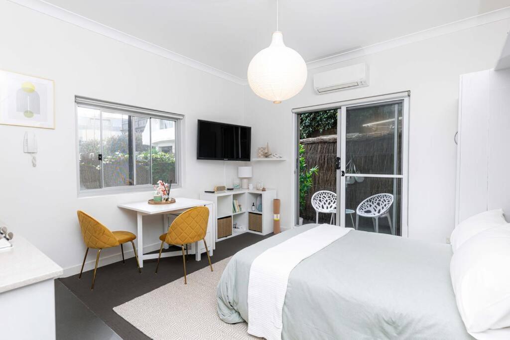 um quarto branco com uma cama, uma mesa e cadeiras em Bright Beachfront Studio with Terrace & Aircon em Sydney