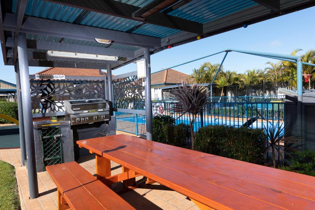 a wooden bench sitting under a pergola next to a pool at Forster Holiday Village in Forster