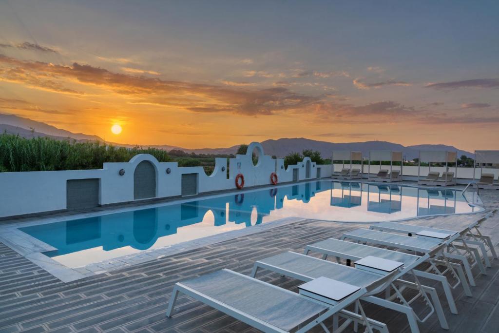 ein Pool mit Stühlen und der Sonnenuntergang im Hintergrund in der Unterkunft Apollo Hotel 1 in Georgioupoli