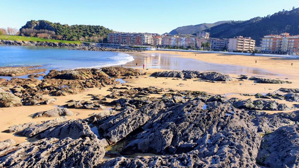 a beach with rocks and the water and buildings at Castro Urdiales in Castro-Urdiales