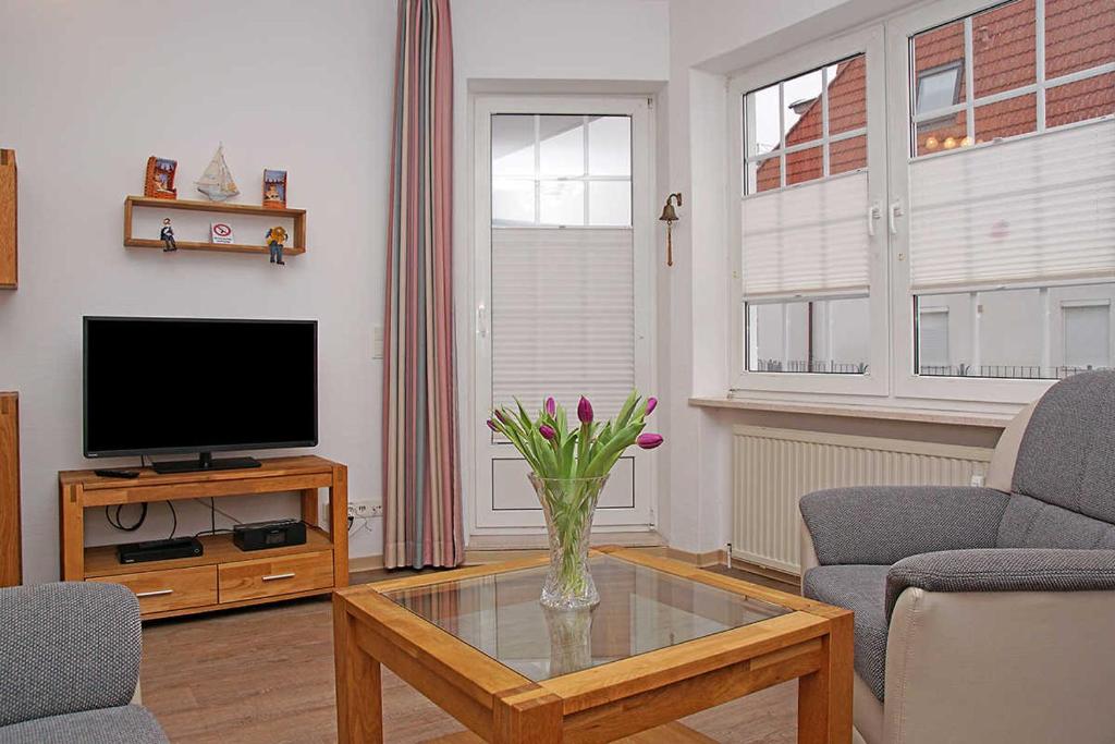 una sala de estar con TV y un jarrón de flores sobre una mesa en Fischerhus _ Wohnung 3 en Cuxhaven