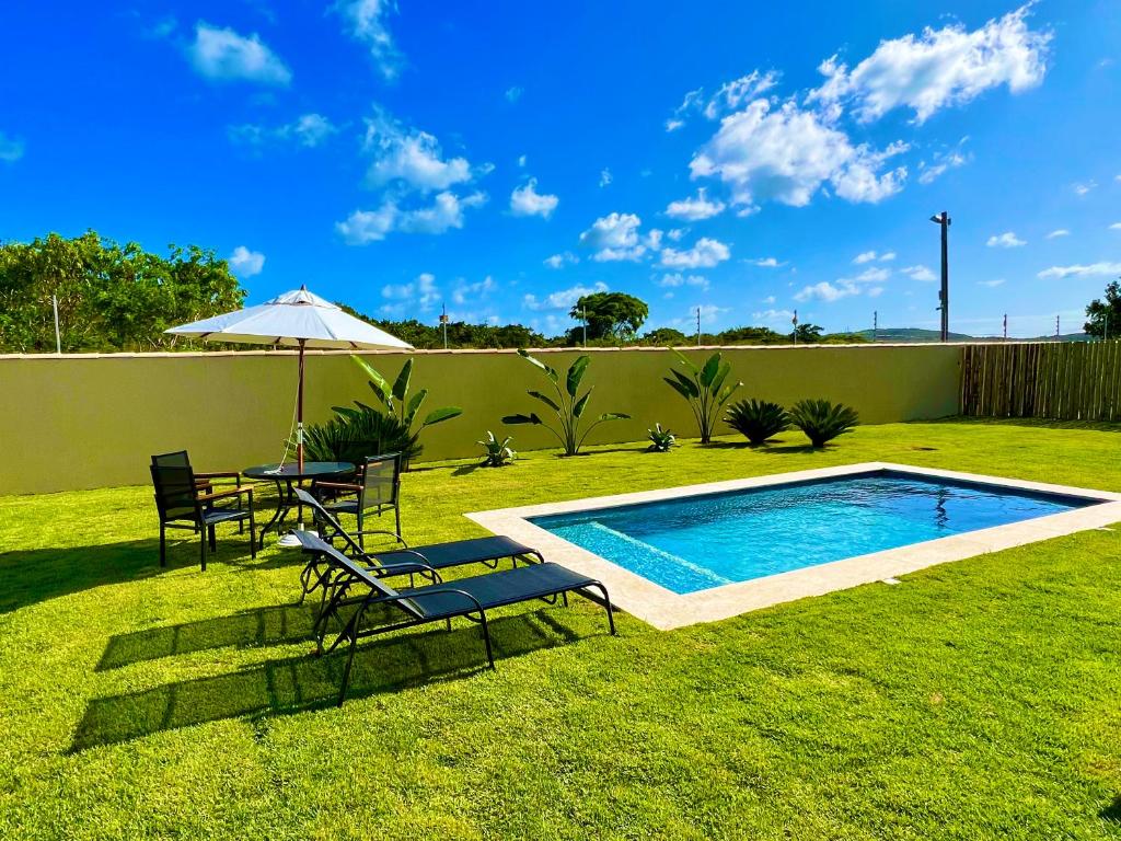 un patio trasero con piscina, sillas y sombrilla en Private House Buzios - casa aluguel, en Búzios