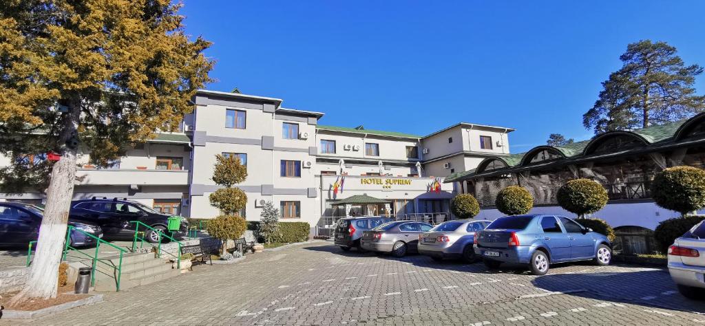 eine Reihe von Autos, die auf einem Parkplatz vor einem Gebäude geparkt sind in der Unterkunft Hotel Suprem in Băile Olăneşti