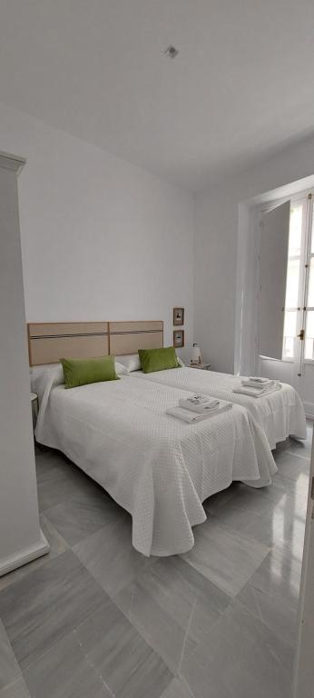 a white bedroom with two beds and a window at el 2 de Flamenco 2ºA in Cádiz