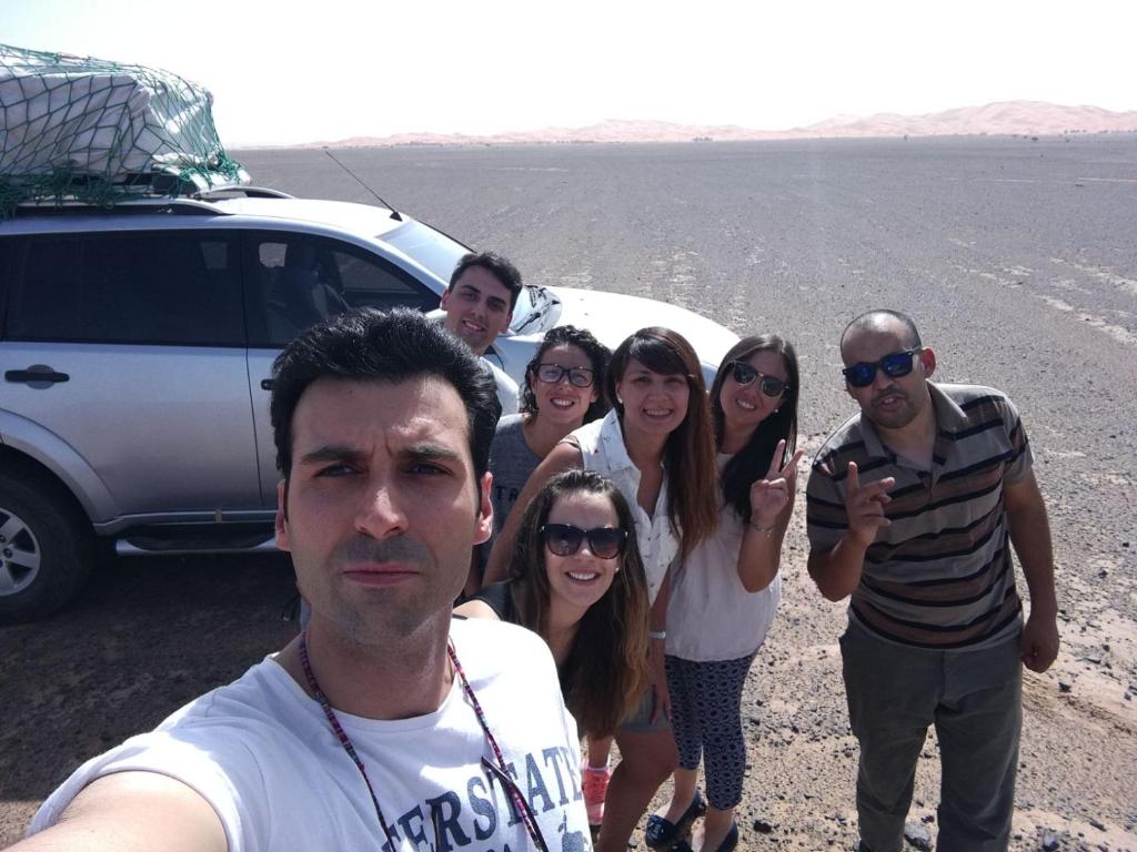 a group of people standing next to a car in the desert at Sahara Desert Camp in Adrouine