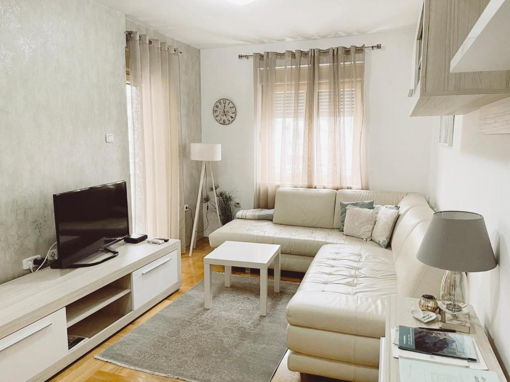 a white living room with a couch and a tv at Aurora Apartment in Podgorica