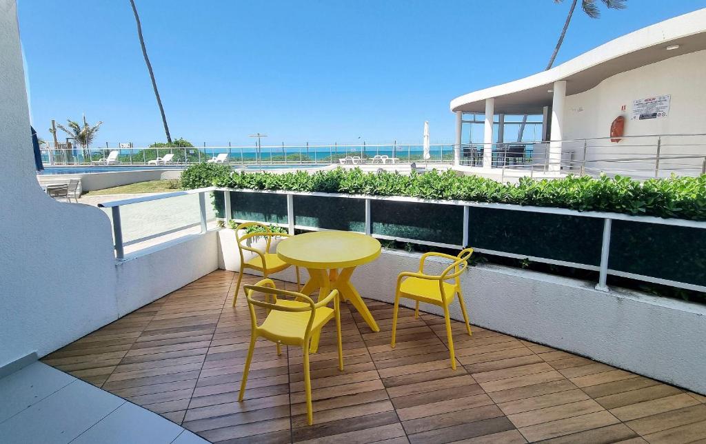 une table et des chaises jaunes sur un balcon donnant sur l'océan dans l'établissement Areias do Mar | 2 Quartos, Terraço e Frente ao Mar A102, à Barra de São Miguel