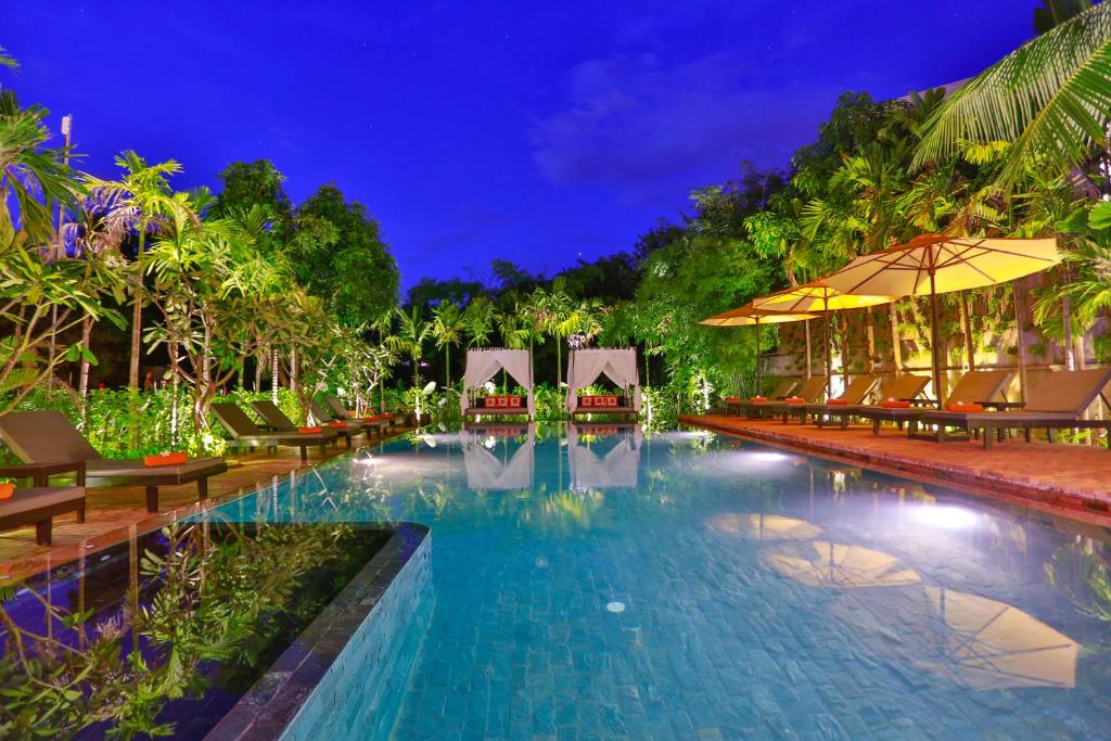 a resort pool with chairs and umbrellas at night at Home Indochine D'angkor Hotel in Siem Reap
