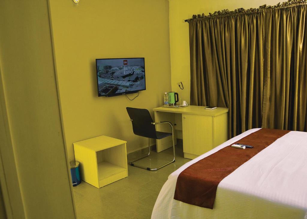 um quarto de hotel com uma cama, uma secretária e uma televisão em TRAVELLERS HOMELY em Ado Ekiti
