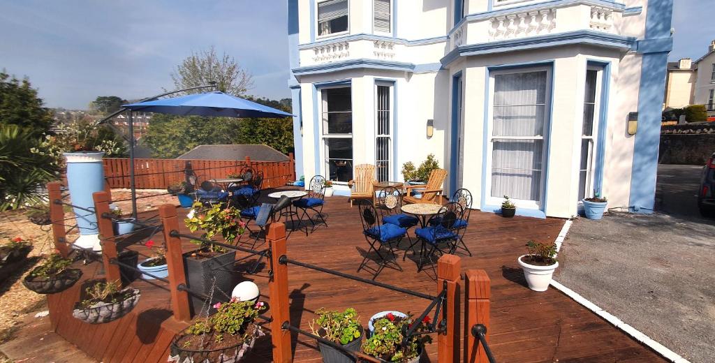 a wooden deck with tables and chairs and an umbrella at Tor Dean Guest House in Torquay