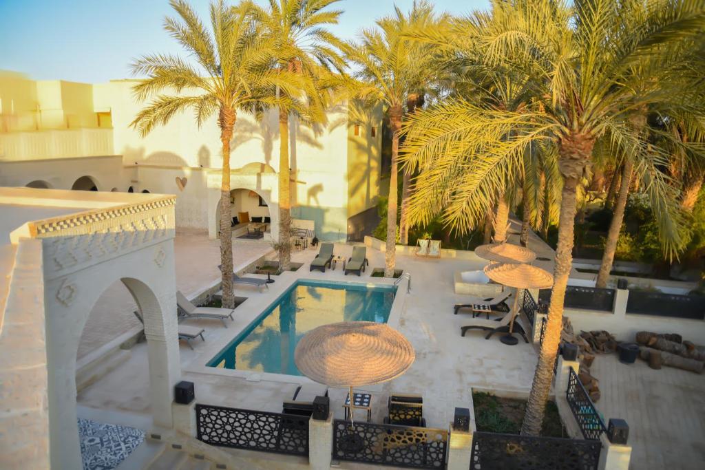 a resort with a pool with palm trees and tables at Dar Yomma in Tozeur