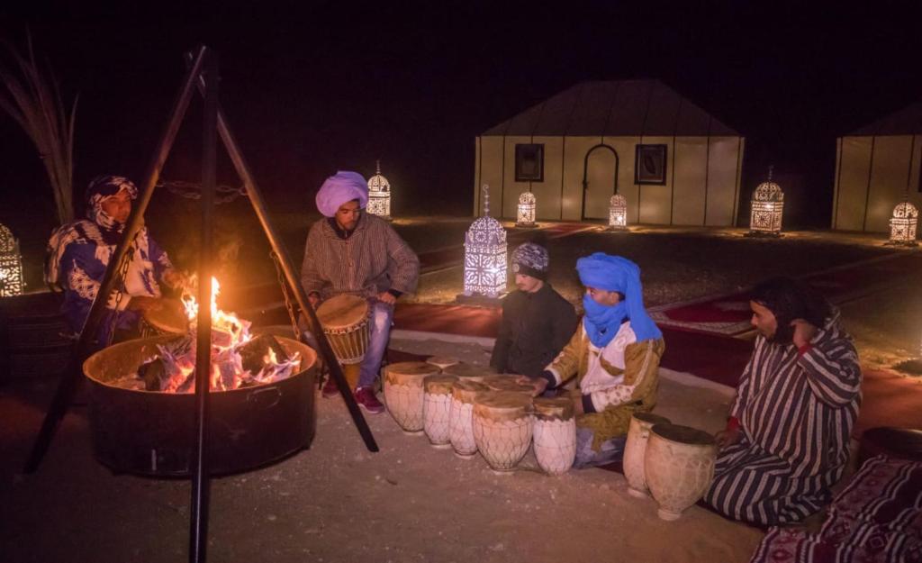 a group of people sitting around a fire at night at Luxury Desert Camp Amanar in Merzouga