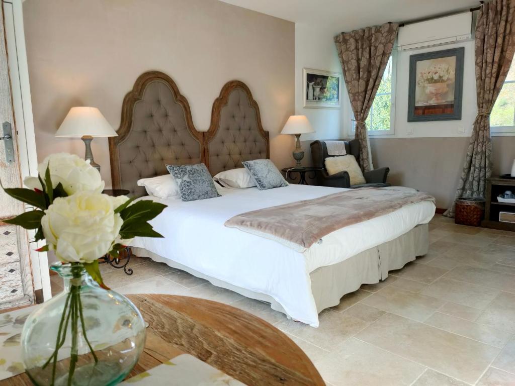Le Clos Bel Ami في Bec-de-Mortagne: غرفة نوم مع سرير و مزهرية من الزهور على طاولة