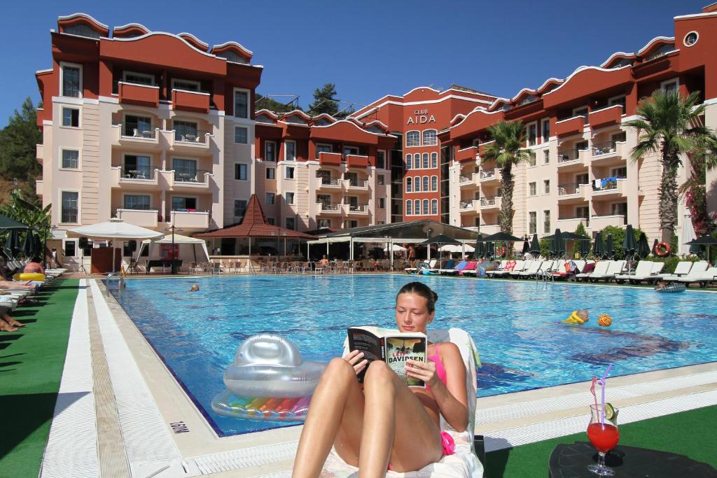 una mujer sentada en una silla leyendo un libro al lado de una piscina en Club Aida en Marmaris
