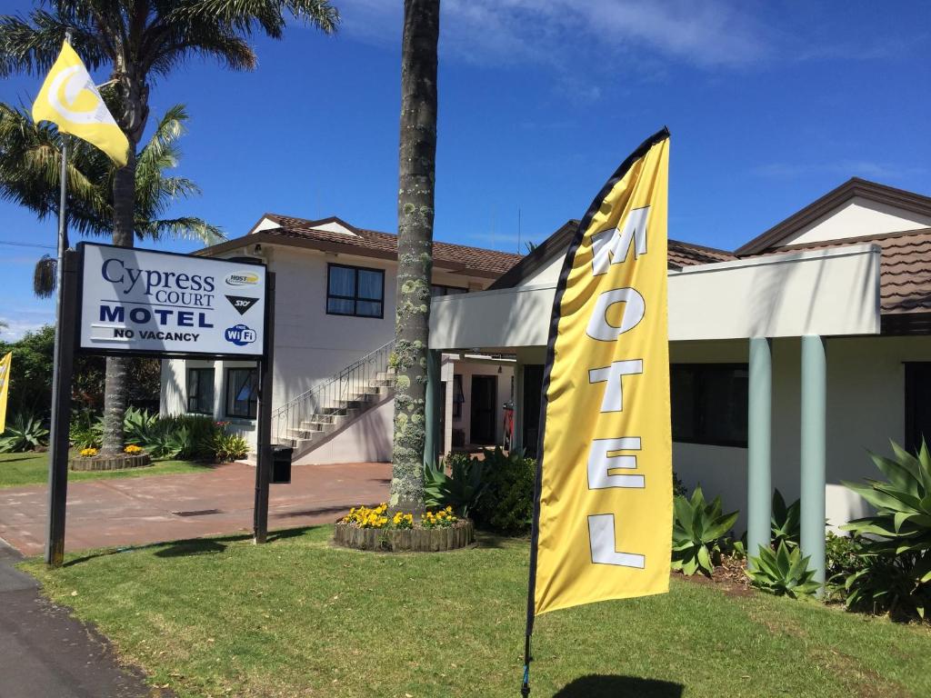 ein Hotelschild und eine gelbe Flagge vor einem Gebäude in der Unterkunft Cypress Court Motel in Whangarei