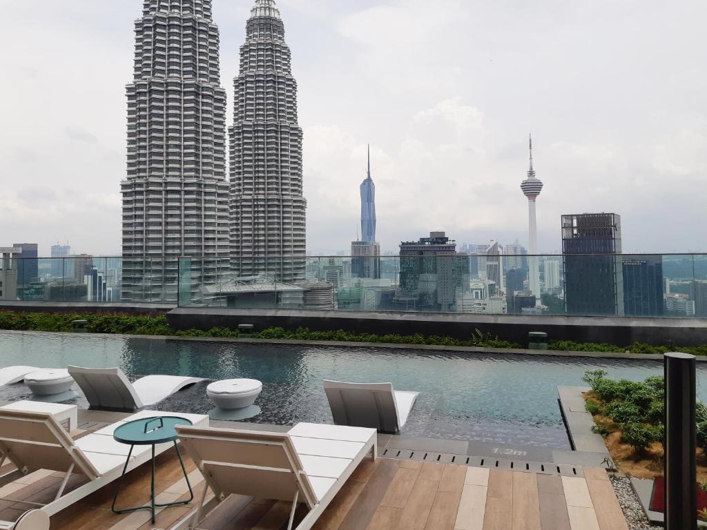 a rooftop patio with chairs and a pool with a city skyline at Star Luxury Suites KLCC in Kuala Lumpur