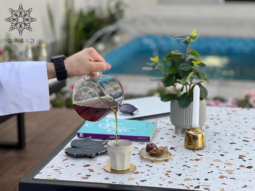 una persona vertiendo vino en una copa sobre una mesa en شاليهات قصيد الفندقية en Buraidah