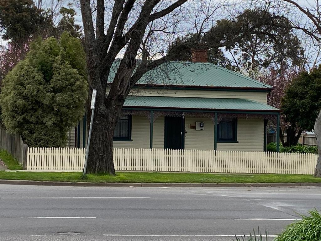 a yellow house with a white fence and a tree at DELIGHTFUL AND CHARMING ROSE COTTAGE in Kilmore