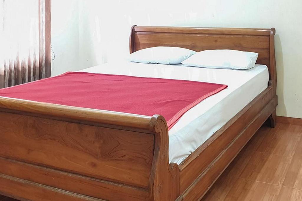 drewniane łóżko z białą pościelą i czerwonym kocem w obiekcie Hotel Bumi Bermi Permai near Bermi Eco Park Mitra RedDoorz w mieście Probolinggo