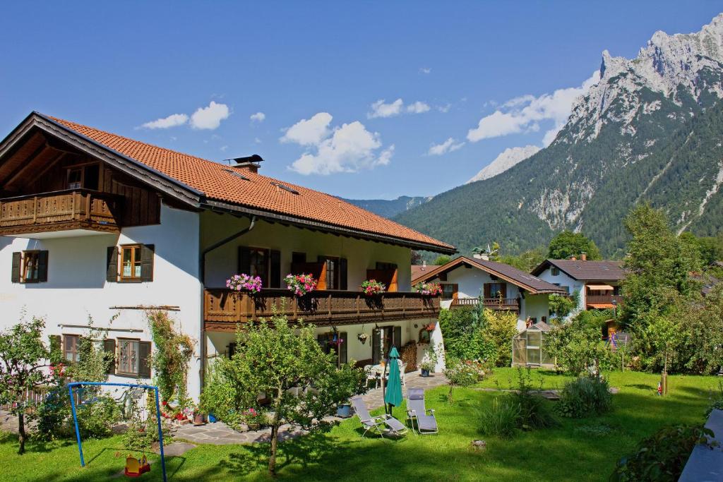 a house with a balcony with a playground and mountains at Gästehaus Kurparkfrieden in Mittenwald