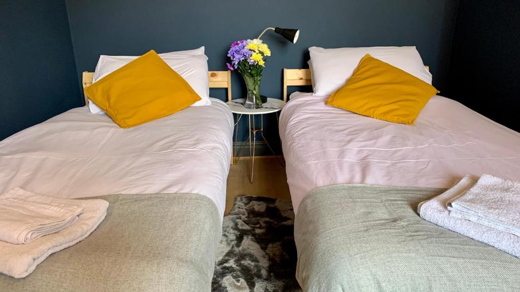 2 Betten mit gelben Kissen und einem Tisch mit einer Blumenvase in der Unterkunft Apartment in City centre, 4 guests, CAR PARK in Doncaster