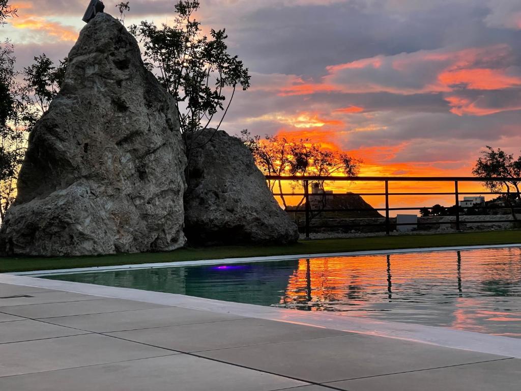 a pool with rocks and a sunset in the background at Daedalium in Marina di Palma