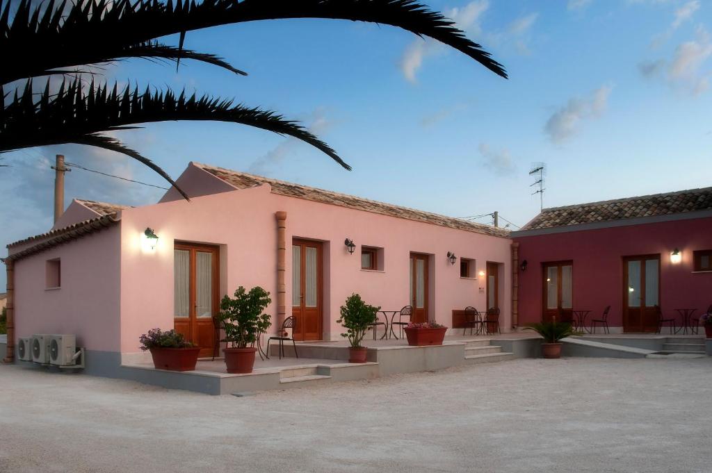 une maison rose avec des plantes en pot dans une cour dans l'établissement Baglio Antico, à Fulgatore