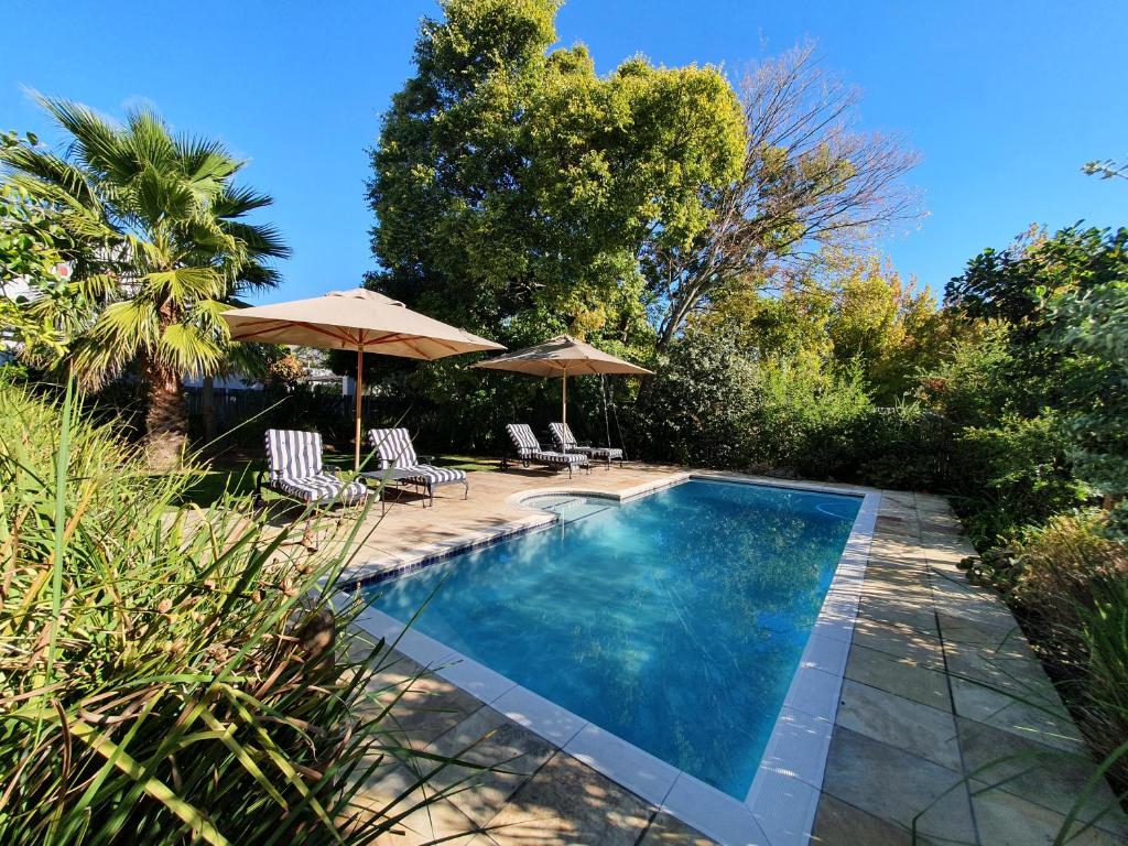 una piscina con due ombrelloni e due sedie di Petit Ermitage a Franschhoek