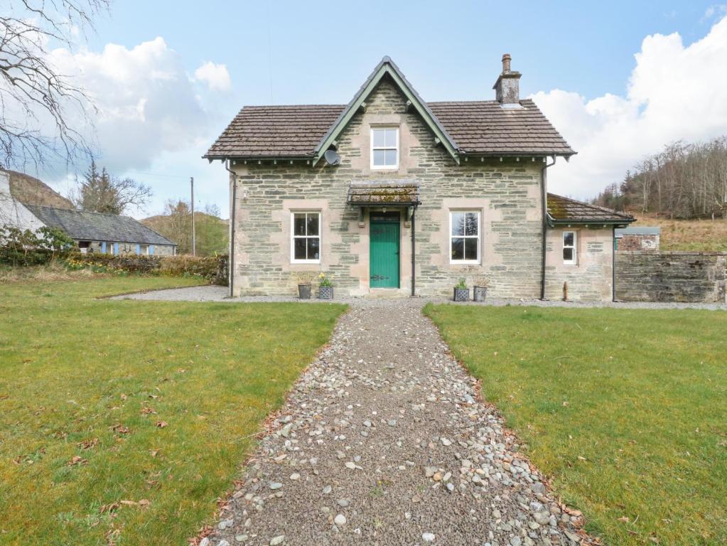 a stone house with a green door and a gravel driveway at The School House in Lochgilphead