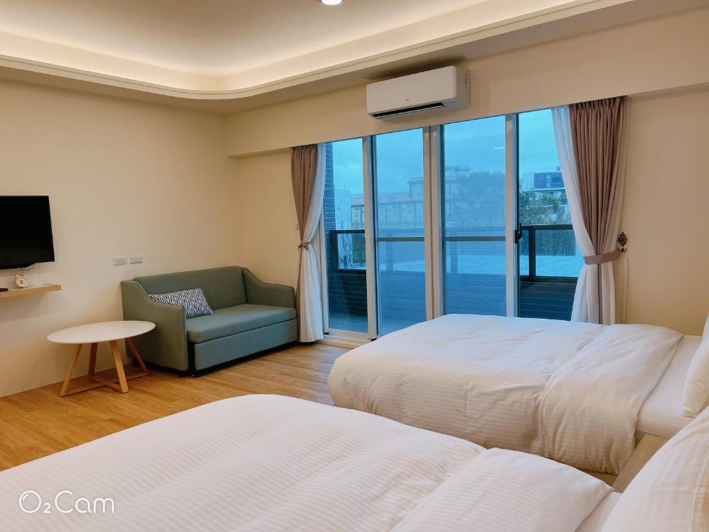 a hotel room with two beds and a chair and a window at Penghu Little Apple II in T'ien-hsiang