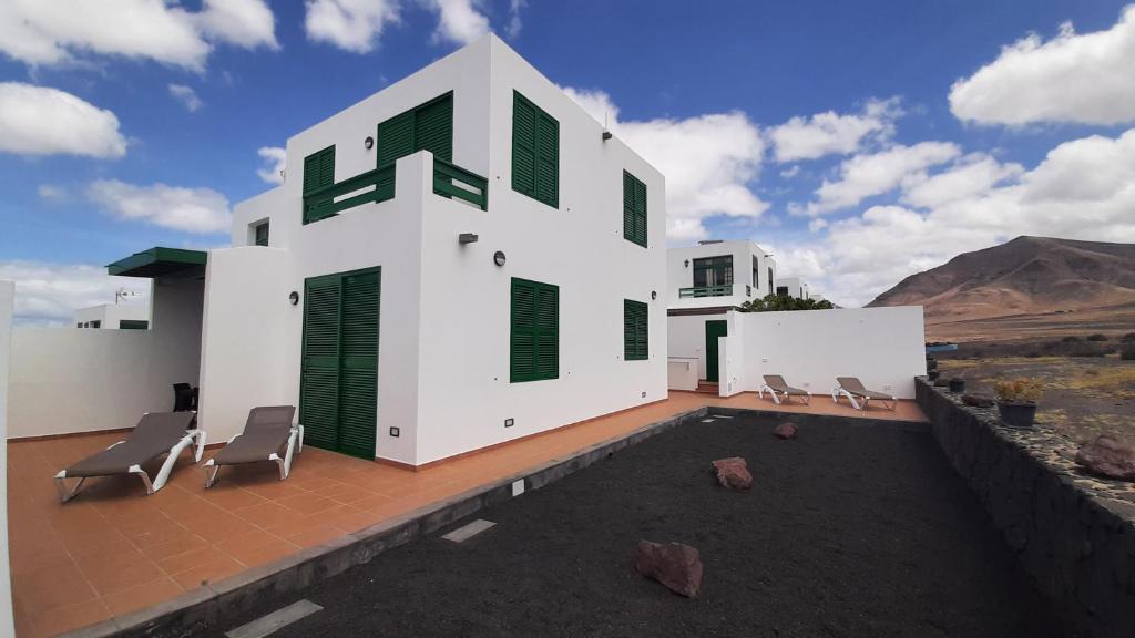 een wit huis met groene luiken en stoelen bij Omae Papagayo in Playa Blanca