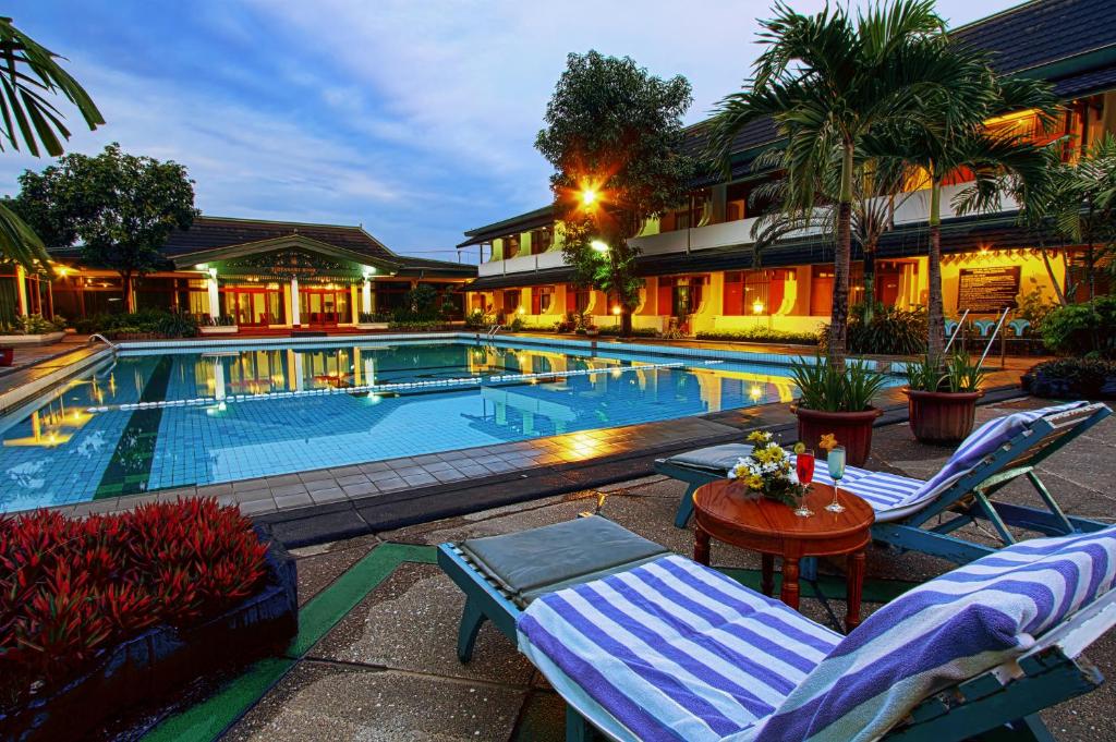a swimming pool with two lounge chairs and a table at Kusuma Sahid Prince Hotel Solo in Solo