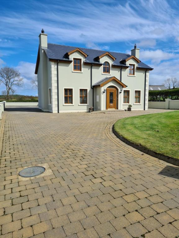 une grande maison blanche avec une allée en briques dans l'établissement Ballyloskey House, à Carndonagh