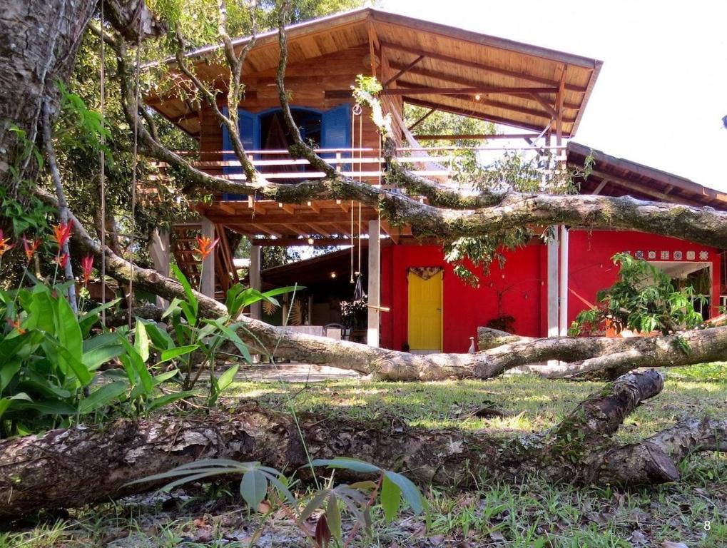 a fallen tree in front of a red house at Casa Estilosa e Rústica com Vista para o Pôr do Sol da Ilha do Mel! in Convento