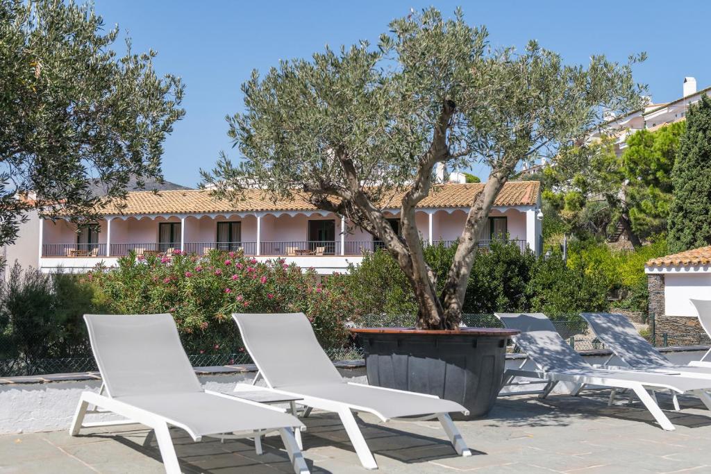 a group of chairs and a tree in front of a building at Hotel Playa Sol in Cadaqués