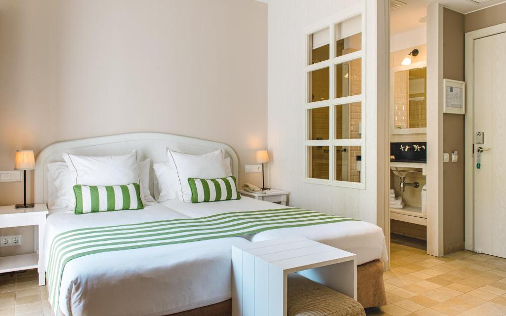 a white bedroom with a large bed with green and white pillows at Hotel Playa Sol in Cadaqués